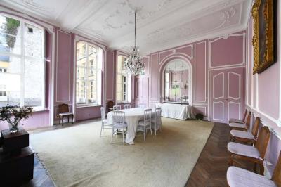 Salle de réception élégante avec tables dressées, chaises blanches, décorations florales et un piano en arrière-plan.