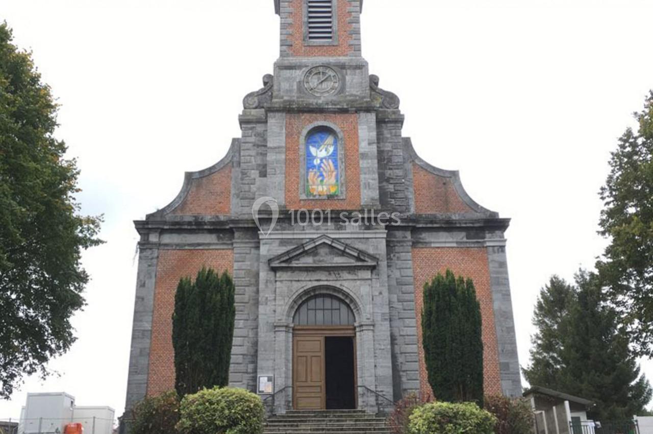 Façade d'une église en briques et pierre avec un vitrail coloré, entourée d'arbres et de buissons.