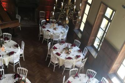 Salle de réception élégante avec tables dressées, chaises blanches, décorations florales et un piano en arrière-plan.