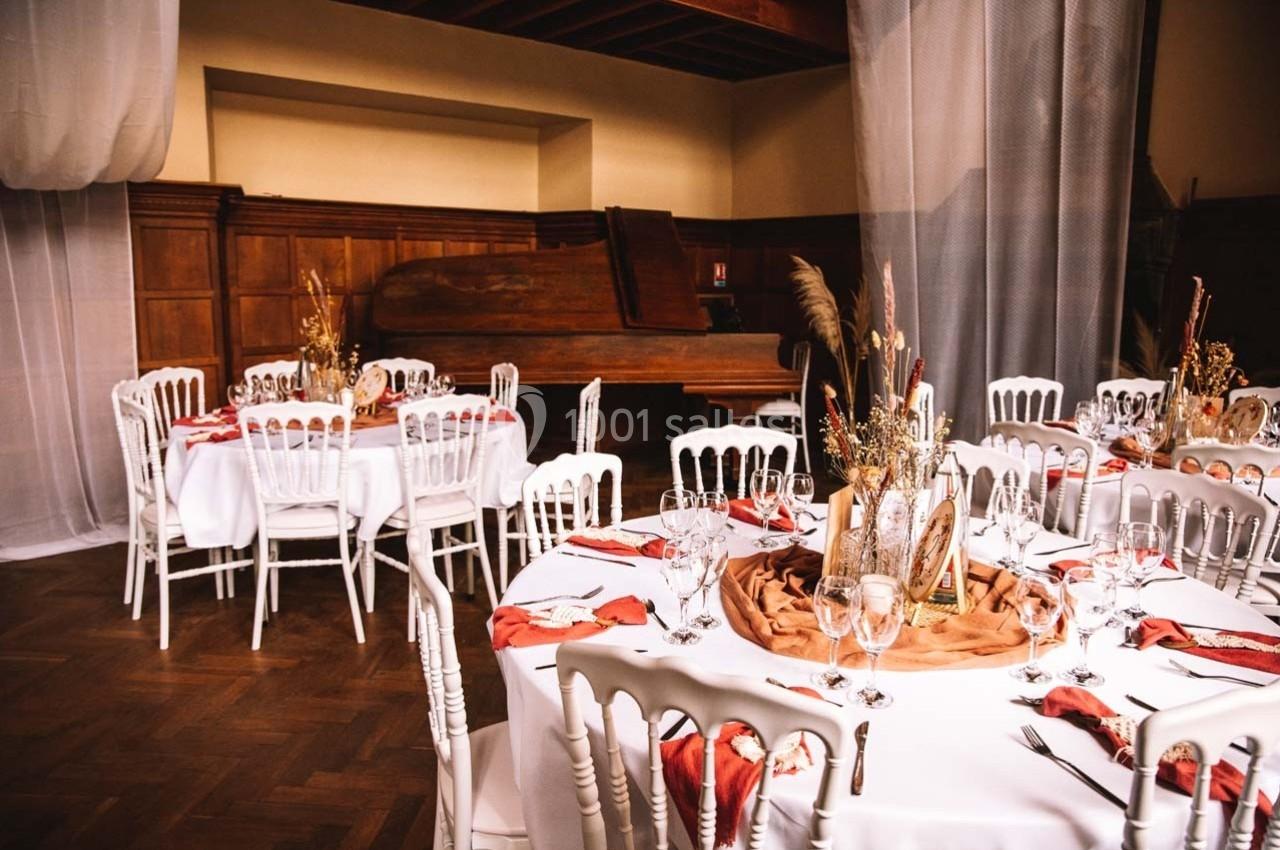 Salle de réception avec tables rondes décorées de nappes blanches, serviettes rouges et centres de table floraux.