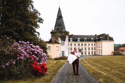 Salle de réception élégante avec tables dressées, chaises blanches, décorations florales et un piano en arrière-plan.