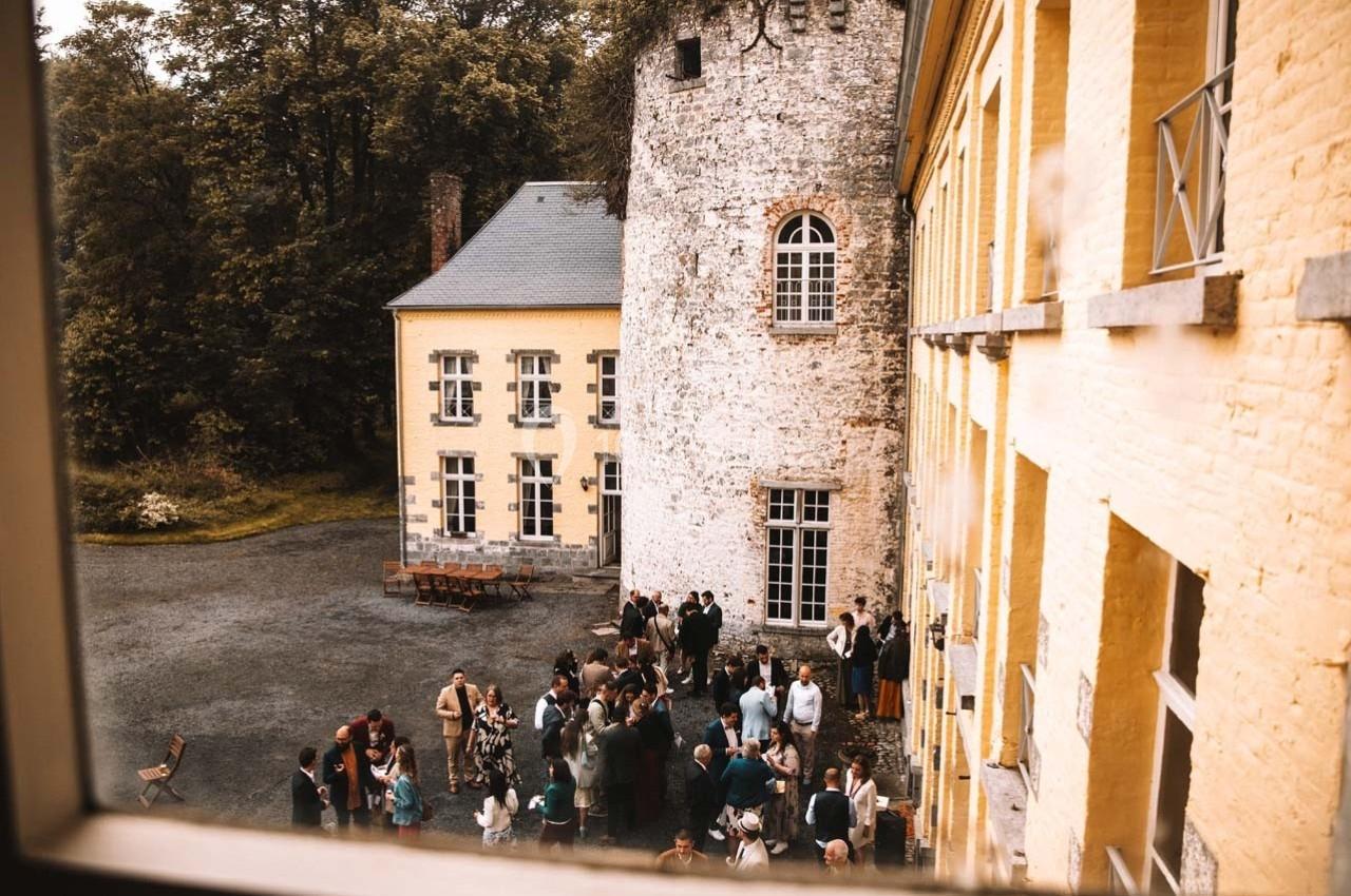 Groupe de personnes rassemblées dans une cour extérieure près d'un bâtiment ancien en pierre et en briques jaunes.