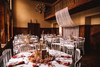 Salle de réception élégante avec tables dressées, chaises blanches, décorations florales et un piano en arrière-plan.