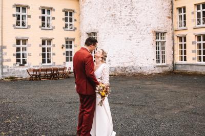 Salle de réception élégante avec tables dressées, chaises blanches, décorations florales et un piano en arrière-plan.