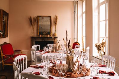 Salle de réception élégante avec tables dressées, chaises blanches, décorations florales et un piano en arrière-plan.