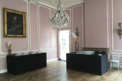 Salle de réception élégante avec tables dressées, chaises blanches, décorations florales et un piano en arrière-plan.