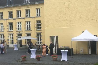 Salle de réception élégante avec tables dressées, chaises blanches, décorations florales et un piano en arrière-plan.