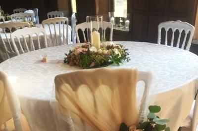 Salle de réception élégante avec tables dressées, chaises blanches, décorations florales et un piano en arrière-plan.