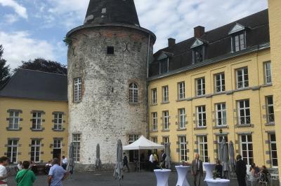 Salle de réception élégante avec tables dressées, chaises blanches, décorations florales et un piano en arrière-plan.