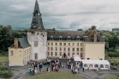 Salle de réception élégante avec tables dressées, chaises blanches, décorations florales et un piano en arrière-plan.