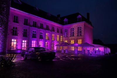 Salle de réception élégante avec tables dressées, chaises blanches, décorations florales et un piano en arrière-plan.