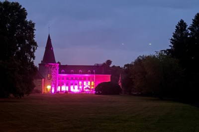 Salle de réception élégante avec tables dressées, chaises blanches, décorations florales et un piano en arrière-plan.