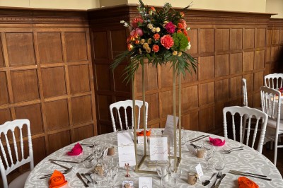 Salle de réception élégante avec tables dressées, chaises blanches, décorations florales et un piano en arrière-plan.