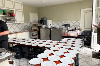 Salle de réception élégante avec tables dressées, chaises blanches, décorations florales et un piano en arrière-plan.