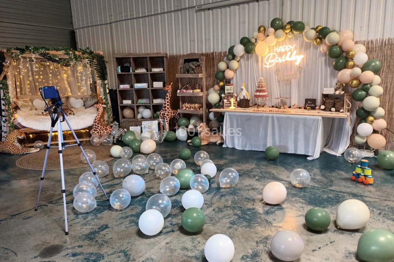 Décoration d'anniversaire avec arche de ballons, table de desserts, guirlandes lumineuses et ballons au sol dans une salle.