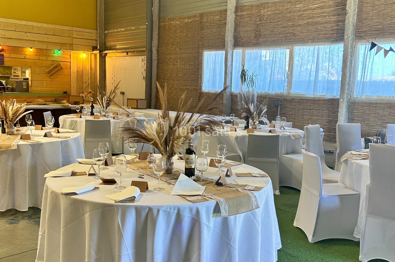 Salle de réception décorée avec des tables rondes dressées, nappes blanches et éléments naturels comme des pampas.