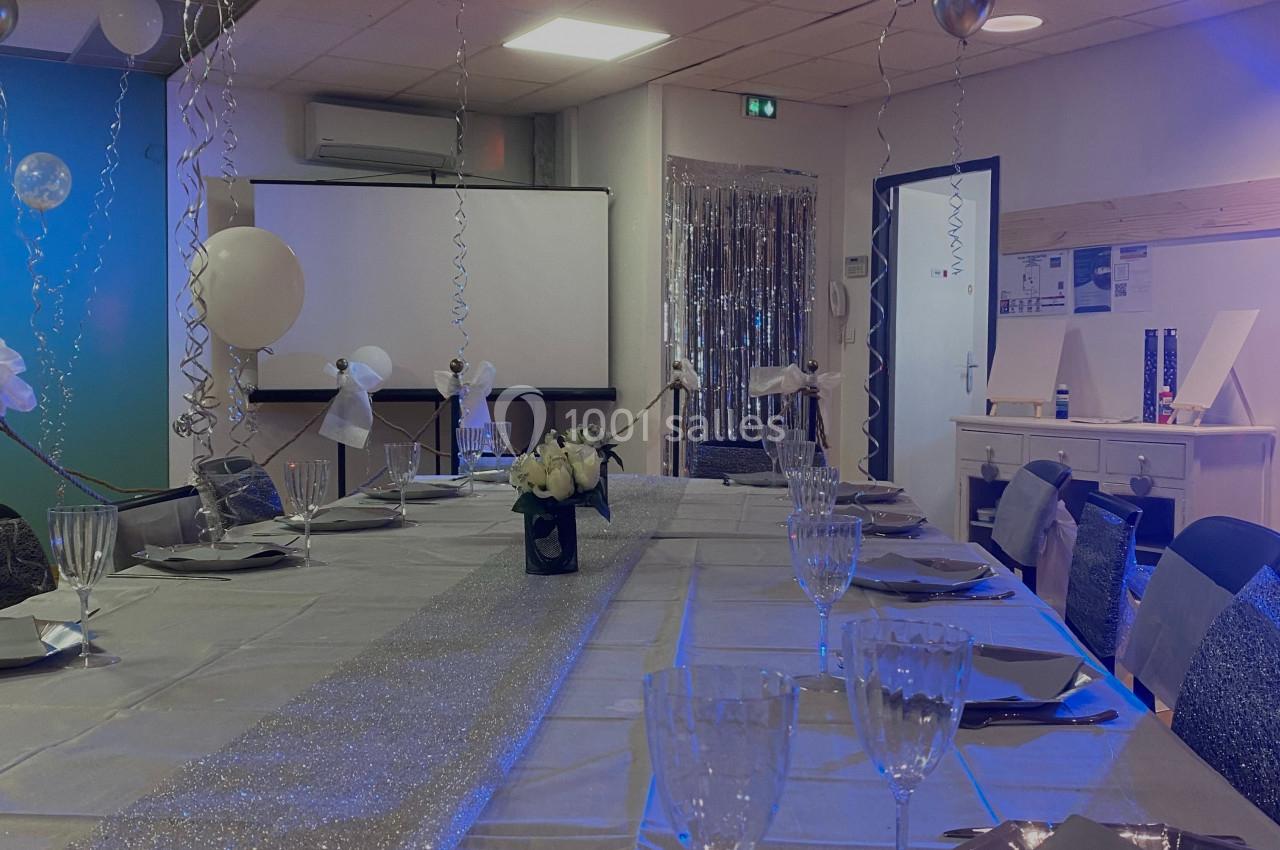 Salle décorée pour un événement avec une longue table dressée, nappes scintillantes, ballons et vaisselle élégante.