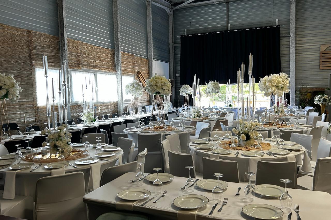 Salle de réception décorée pour un événement, avec des tables dressées, des chandeliers et des compositions florales…