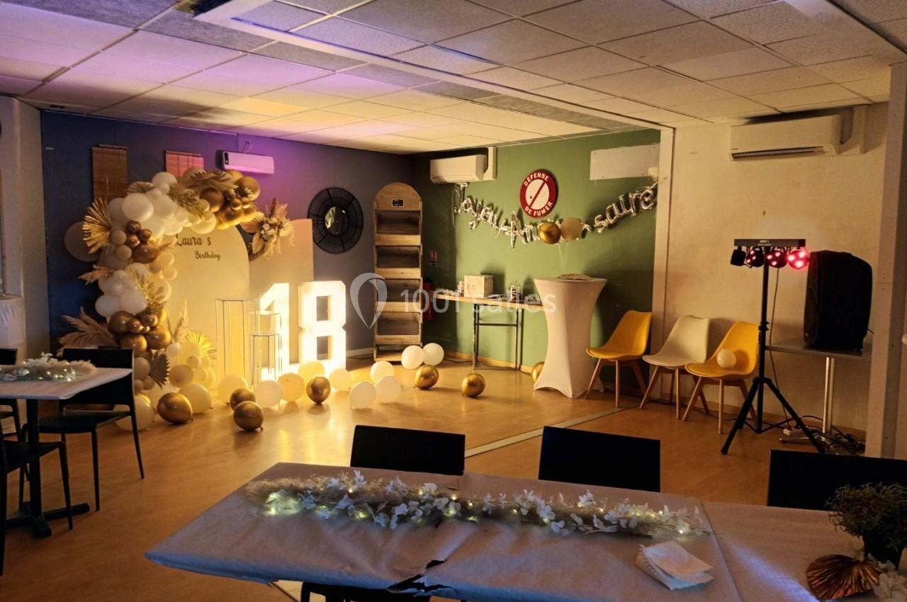 Salle décorée pour un 18e anniversaire avec ballons dorés et blancs, guirlandes lumineuses et tables dressées.