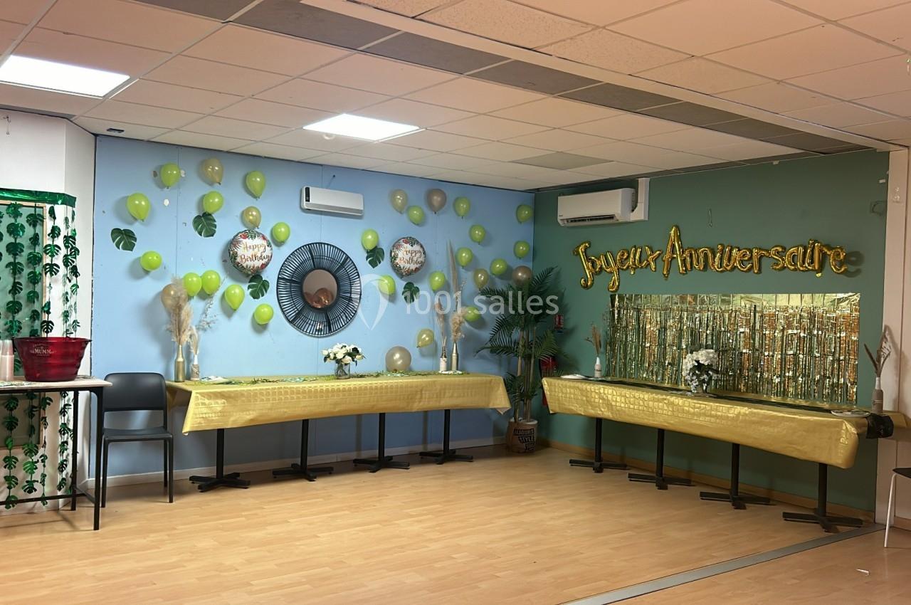Salle décorée pour un anniversaire avec ballons jaunes, guirlandes dorées et tables recouvertes de nappes dorées.