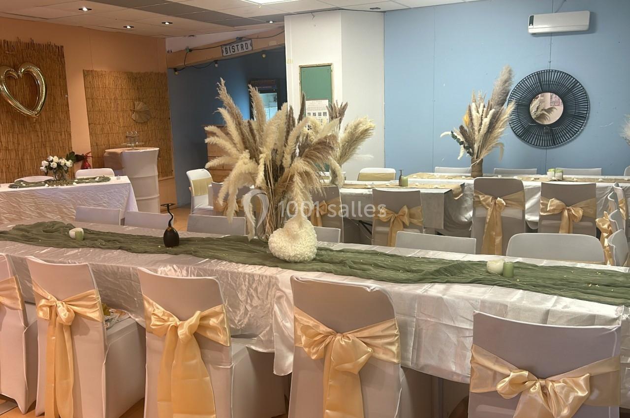 Salle décorée pour un événement avec des tables alignées, nappes blanches, rubans beige et bouquets de pampas.