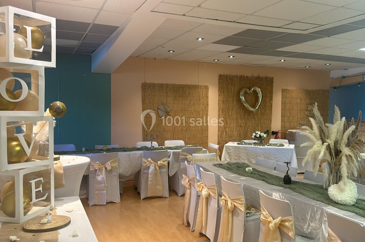Salle décorée pour un événement avec des tables habillées de nappes blanches, des chaises ornées de nœuds dorés et des…