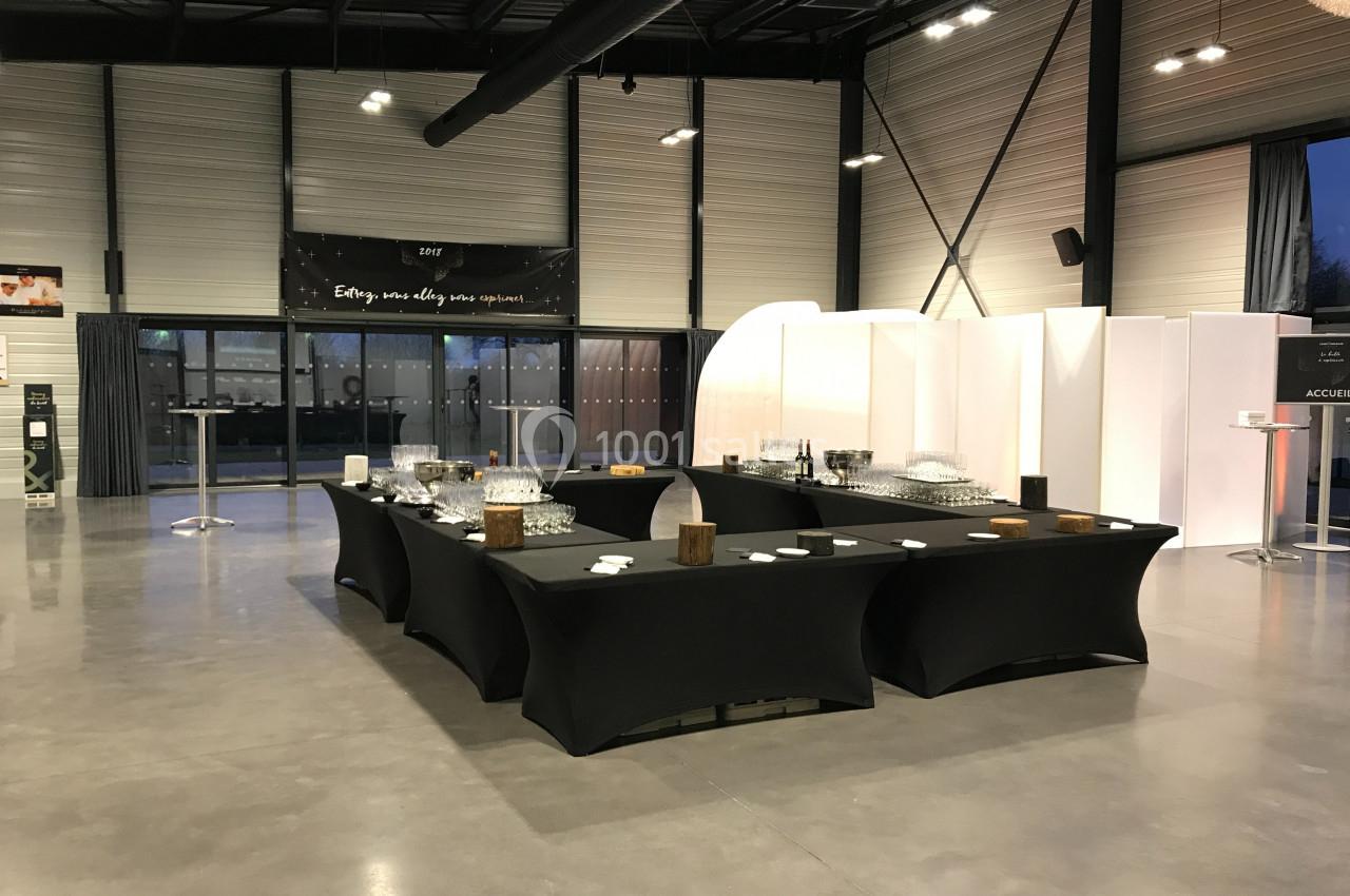 Tables noires dressées avec des verres et des assiettes dans une grande salle lumineuse et moderne.