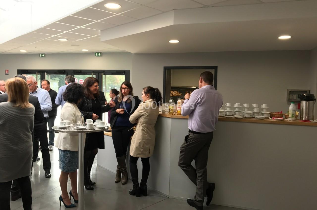 Personnes discutant debout dans un espace de pause avec boissons, tasses et comptoir en arrière-plan.