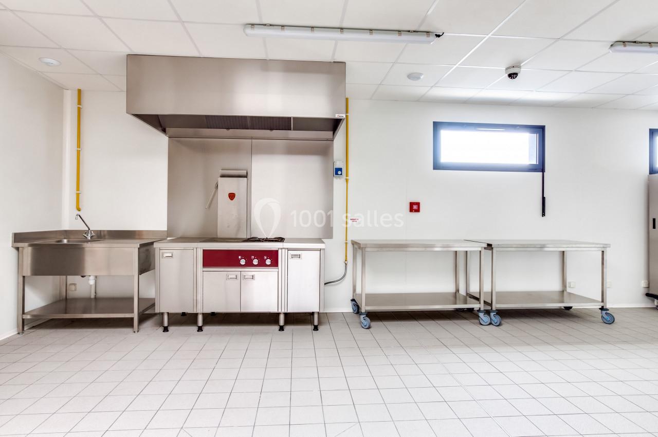 Cuisine professionnelle avec évier, hotte en inox, plan de travail sur roulettes et carrelage au sol.