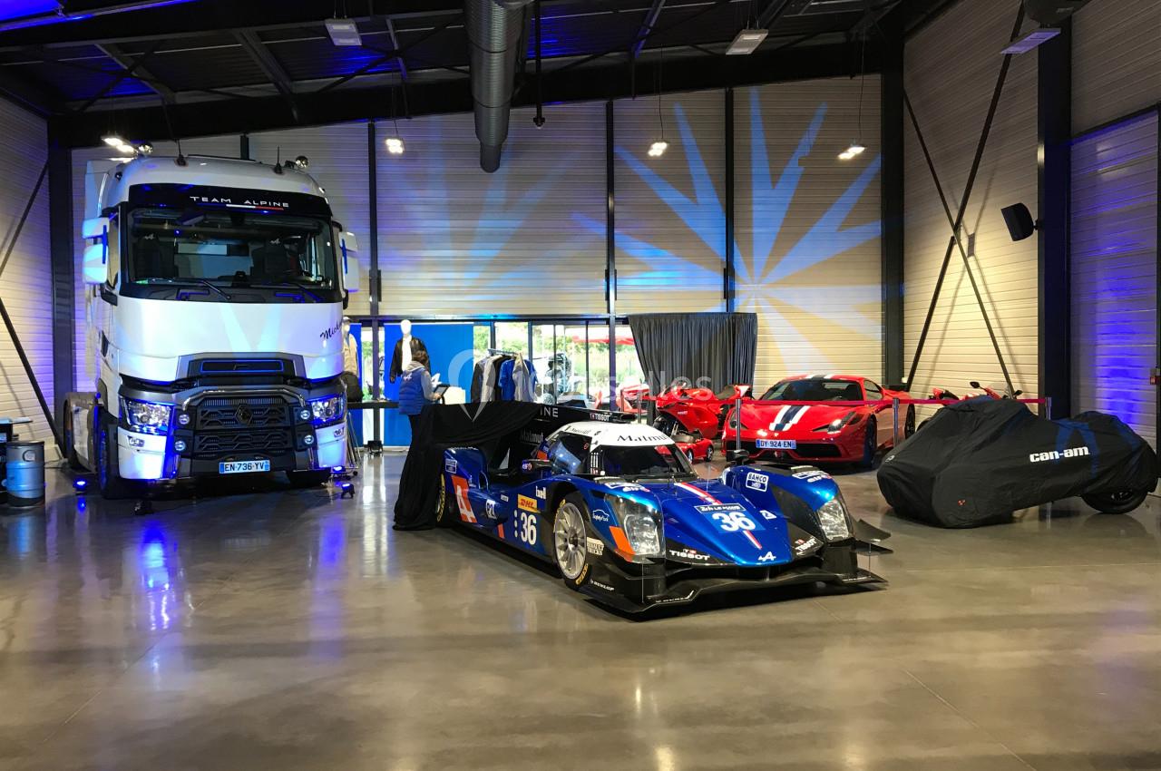 Voitures de sport, camion et véhicules couverts exposés dans un espace intérieur moderne avec éclairage bleu.