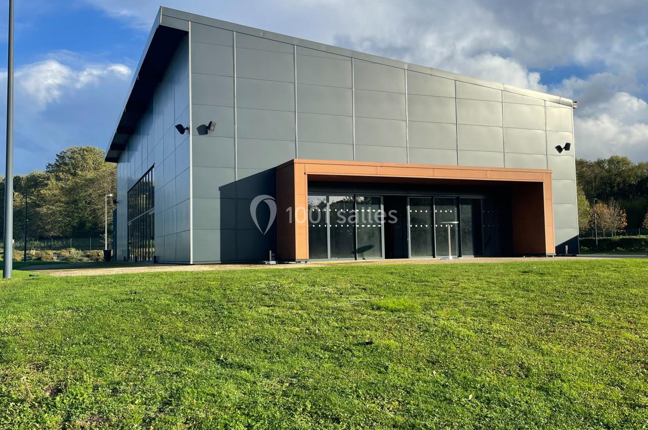 Bâtiment moderne avec façade métallique grise, grandes baies vitrées et encadrement en bois, entouré de pelouse.
