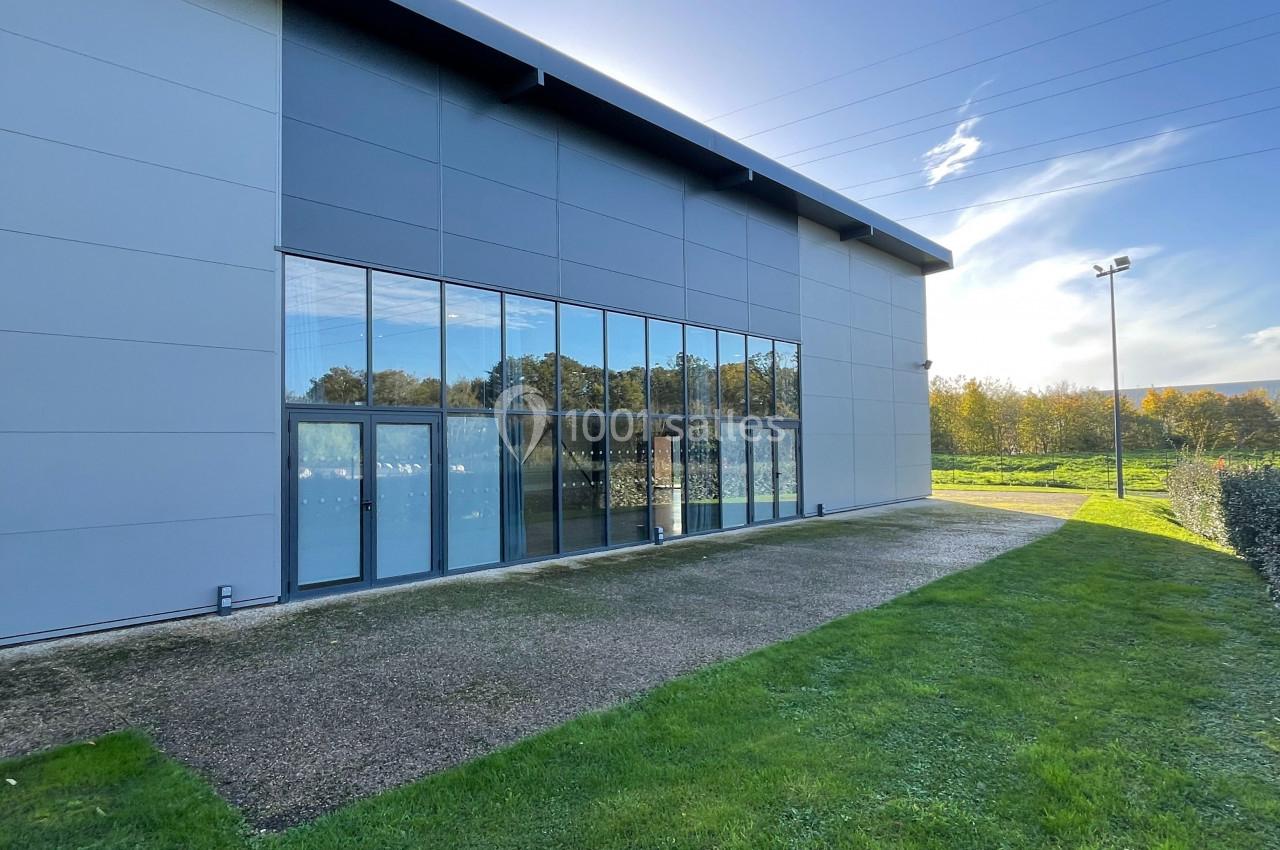 Façade vitrée d’un bâtiment moderne entouré de pelouse, sous un ciel ensoleillé.