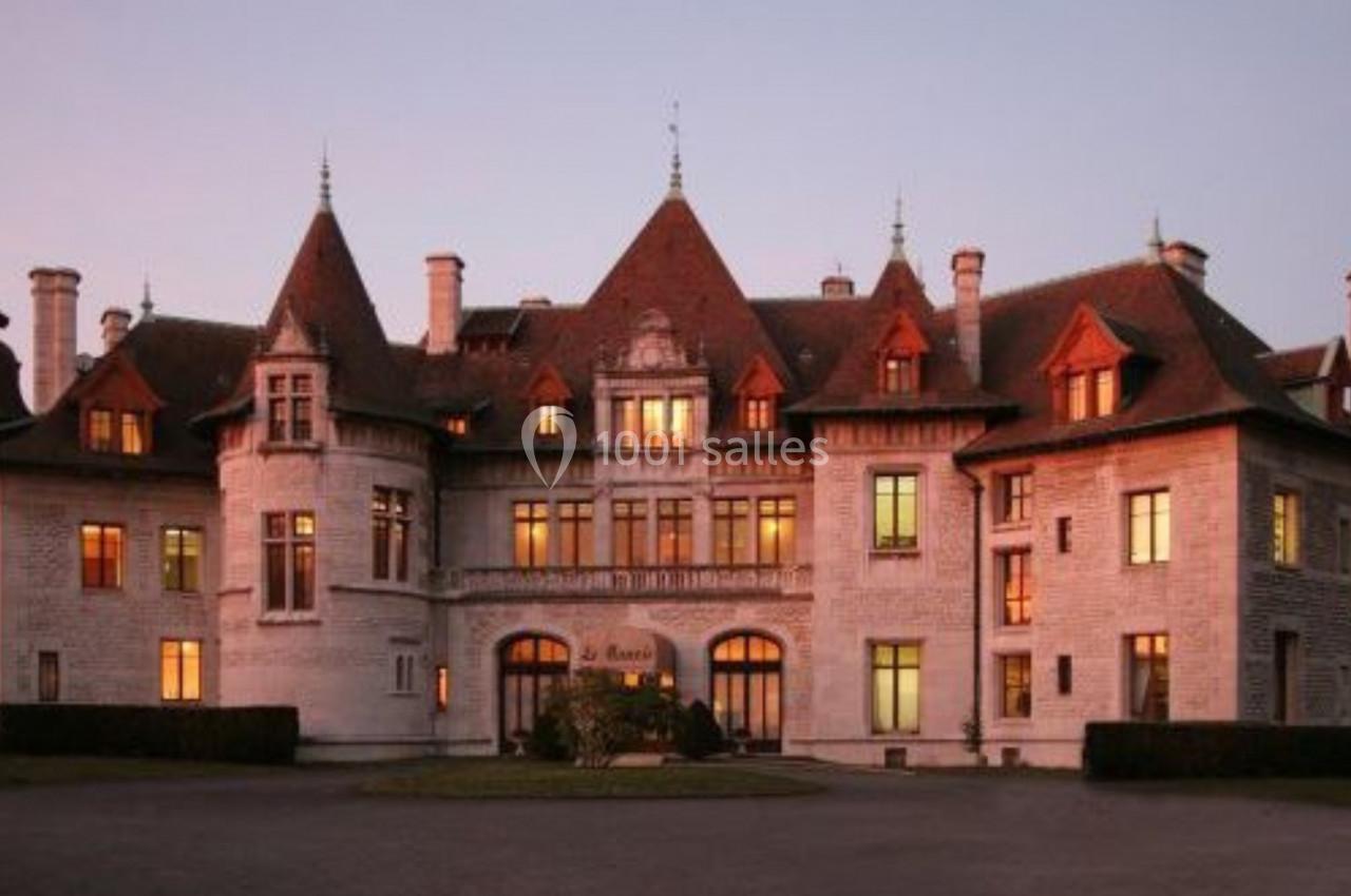Façade d'un grand château en pierre blanche avec des toits en pente, éclairé par une lumière de coucher de soleil.