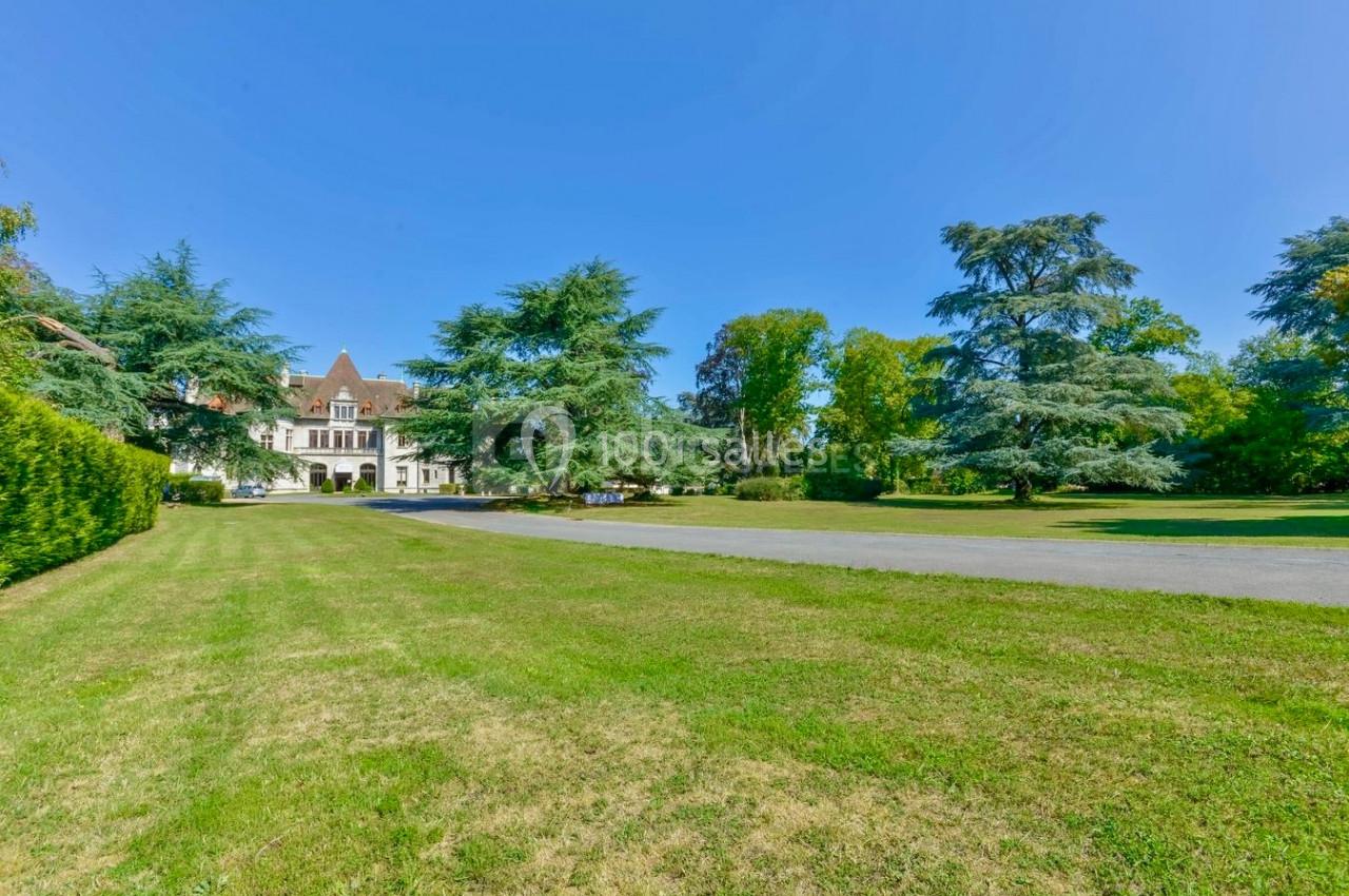 Pelouse verdoyante avec allée menant à un grand bâtiment entouré d'arbres sous un ciel dégagé.