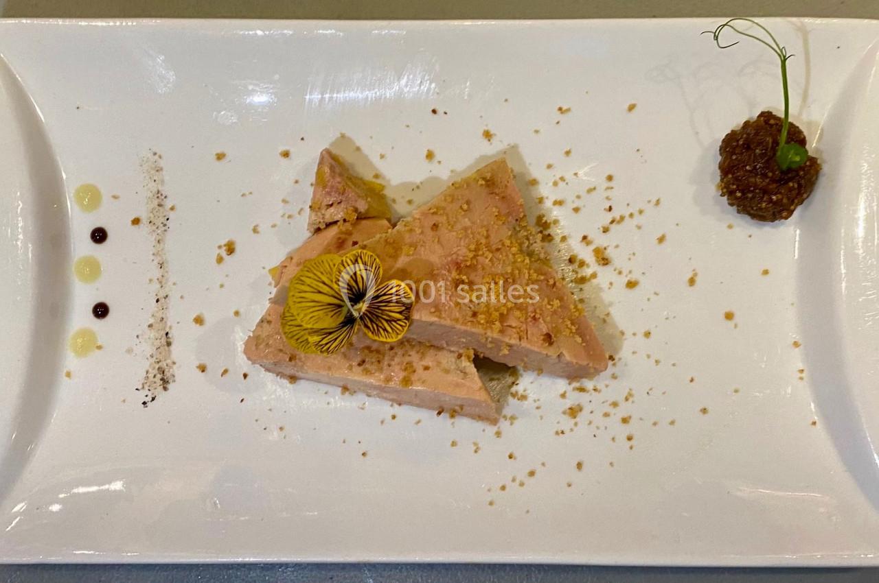 Tranches de foie gras décorées d'une fleur comestible, accompagnées de condiments sur une assiette blanche.