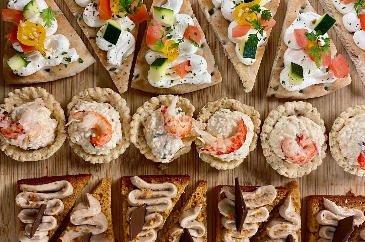Plateau de canapés variés comprenant bouchées salées, tartines garnies et mini-brioches sur une planche en bois.
