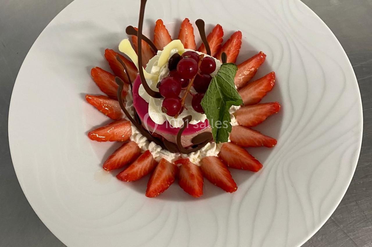 Dessert décoratif avec fraises tranchées, crème, groseilles, feuilles de menthe et éléments en chocolat sur une assiette…