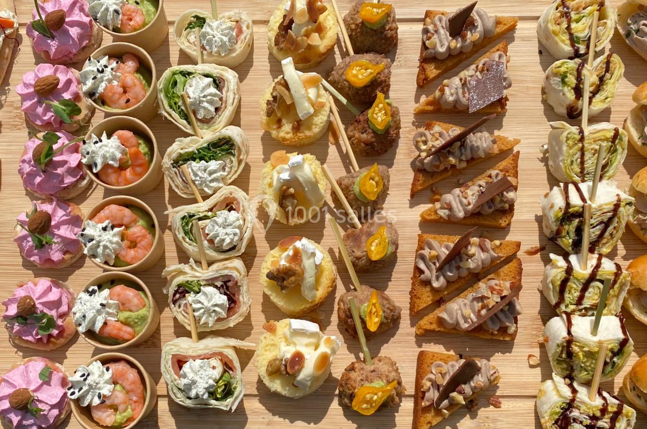 Plateau de bouchées variées comprenant canapés, roulés, mini-sandwichs et amuse-bouches colorés sur une table en bois.