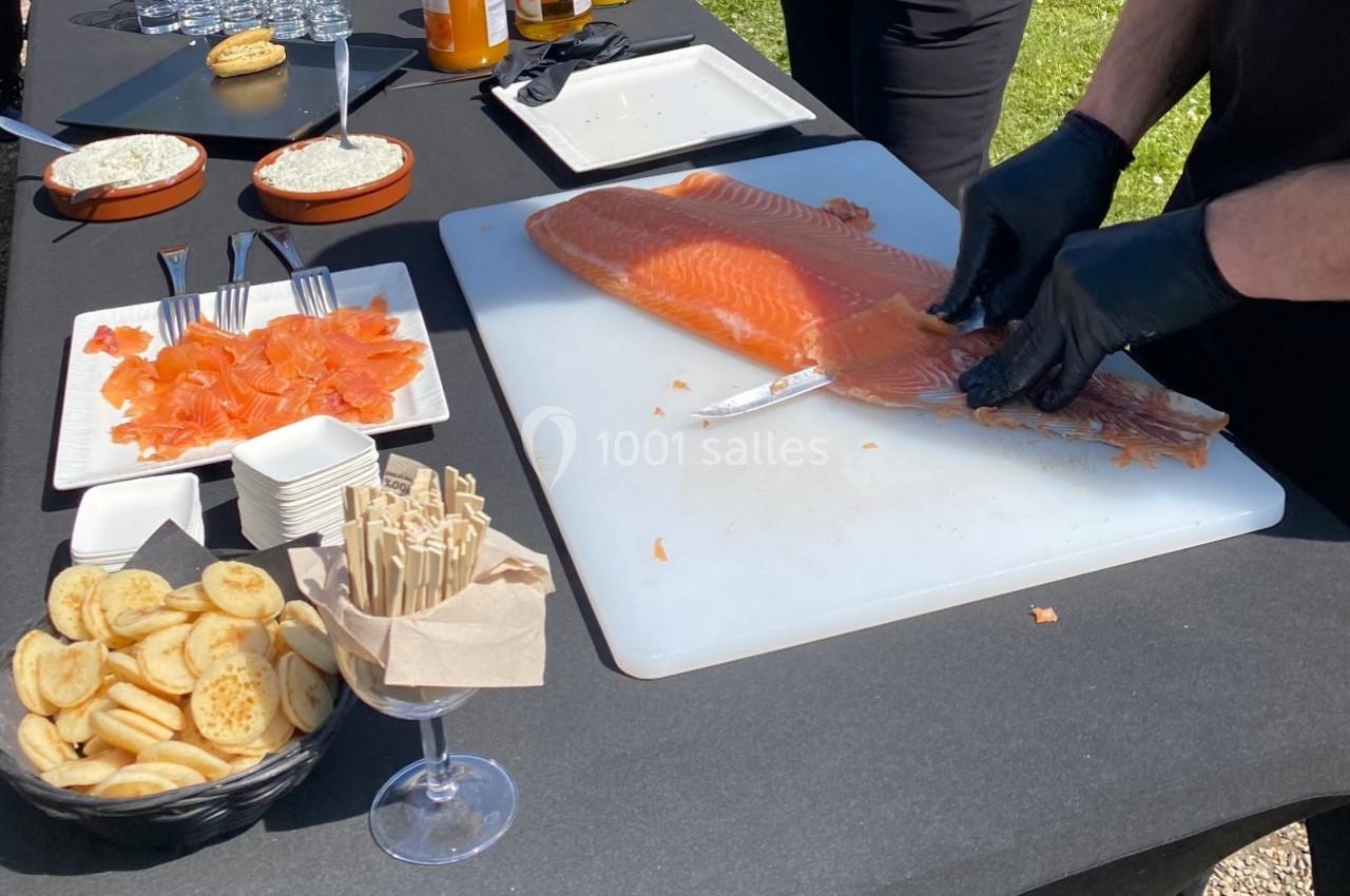 Un chef découpe un filet de saumon frais sur une planche, entouré de toasts et d'accompagnements sur une table.