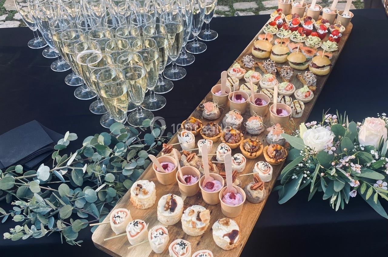 Plateau de bouchées apéritives variées avec flûtes de champagne alignées sur une table noire décorée de feuillage et fleurs.