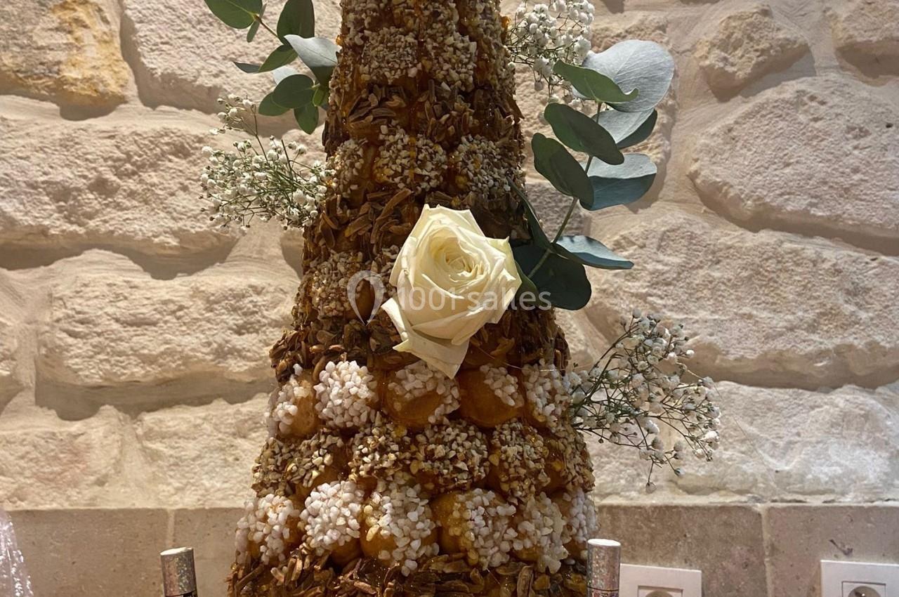 Pièce montée en choux caramélisés décorée de roses blanches et de feuillages, posée sur une table en bois.