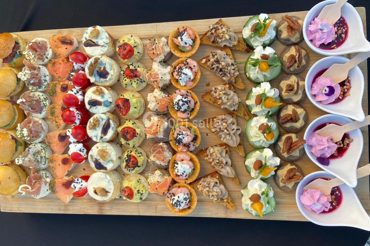 Plateau en bois garni d'un assortiment de bouchées salées et verrines sucrées, disposées en rangées colorées.