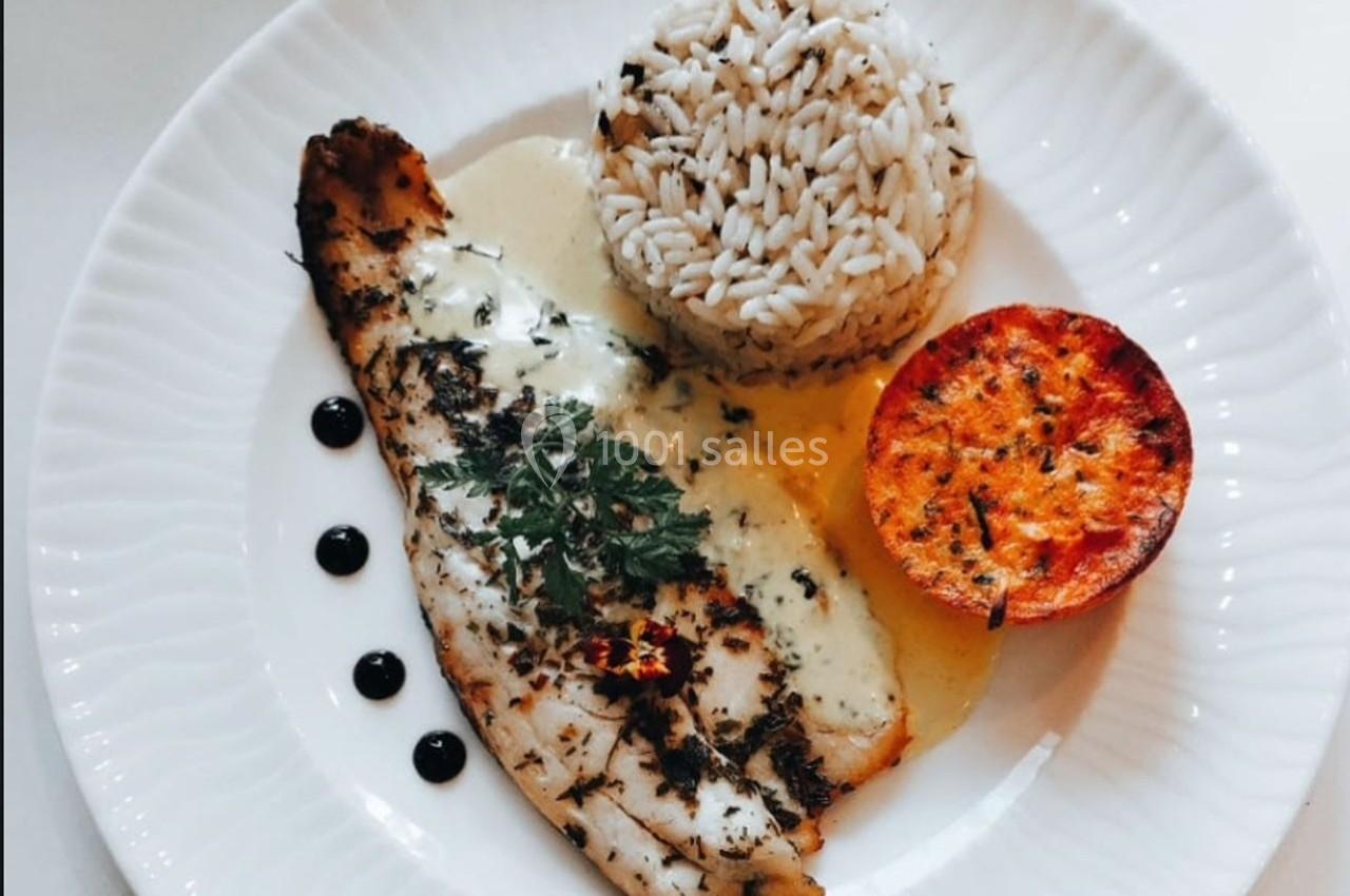 Assiette contenant un filet de poisson grillé, du riz, une demi-tomate rôtie et une sauce crémeuse, décorée de gouttes de…
