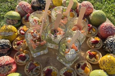 Plateau de verrines et amuse-bouches colorés disposés sur une planche en bois, en extérieur sur une pelouse.