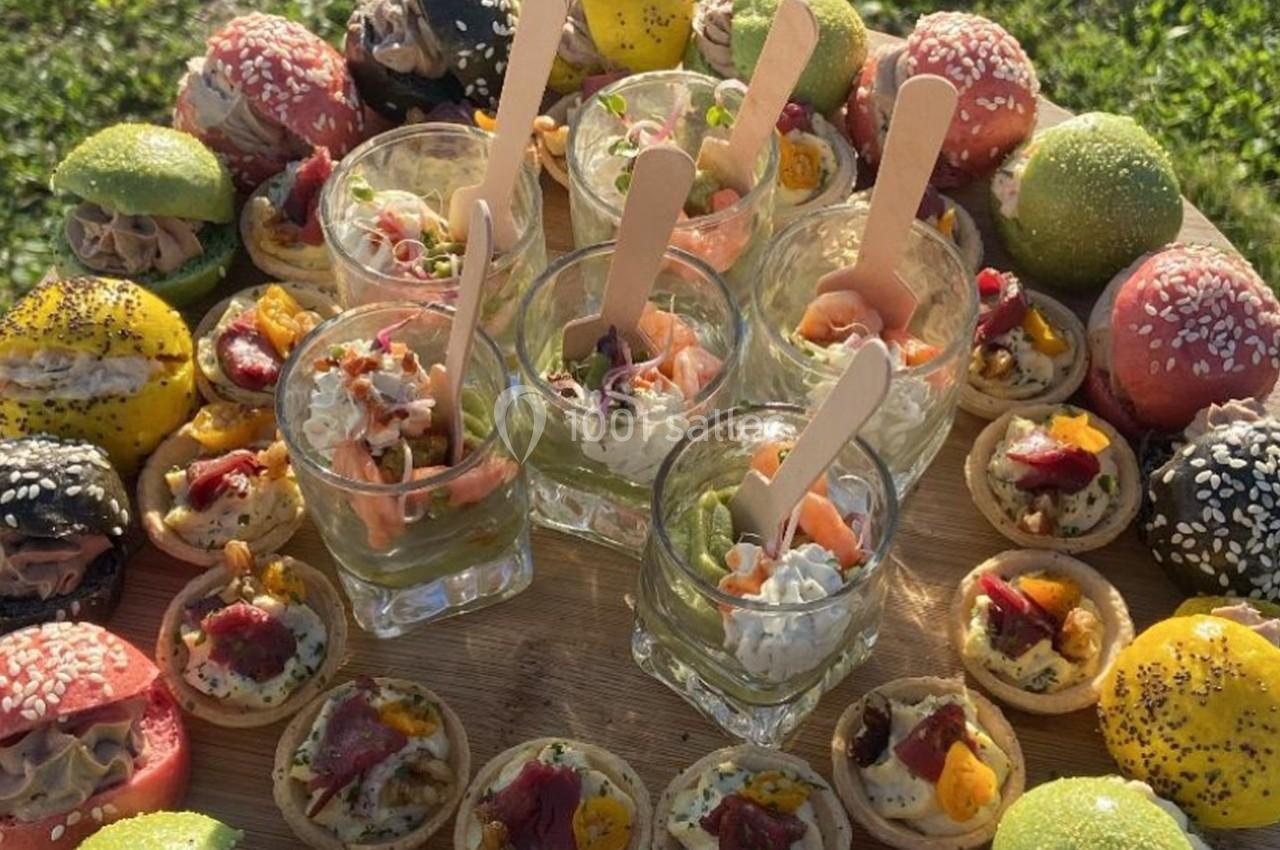 Plateau de verrines et amuse-bouches colorés disposés sur une planche en bois, en extérieur sur une pelouse.