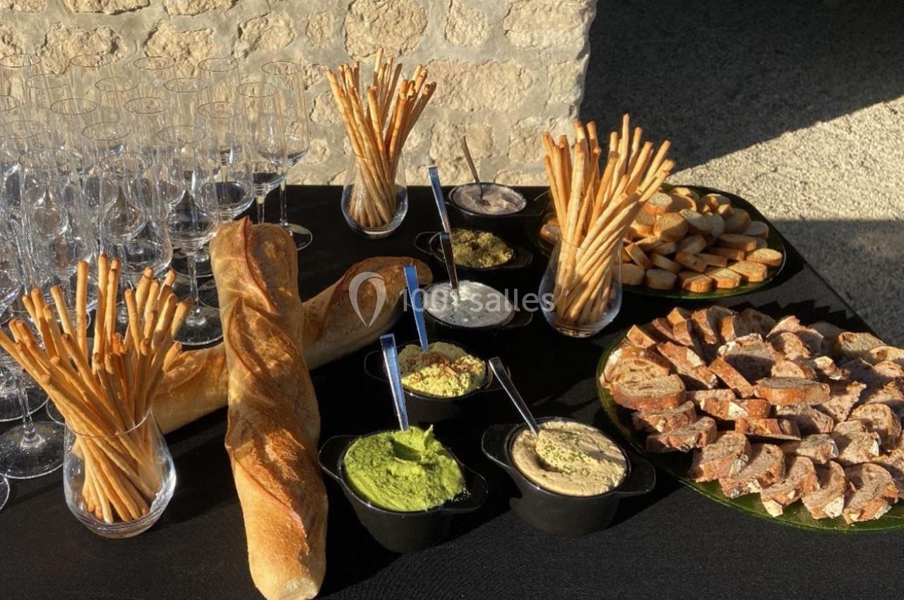 Table avec baguettes, gressins, tranches de pain, sauces variées et verres vides, disposée en extérieur sur une nappe noire.