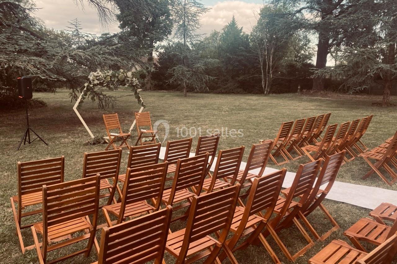 Chaises en bois disposées en rangées devant une arche décorée de fleurs dans un jardin verdoyant.