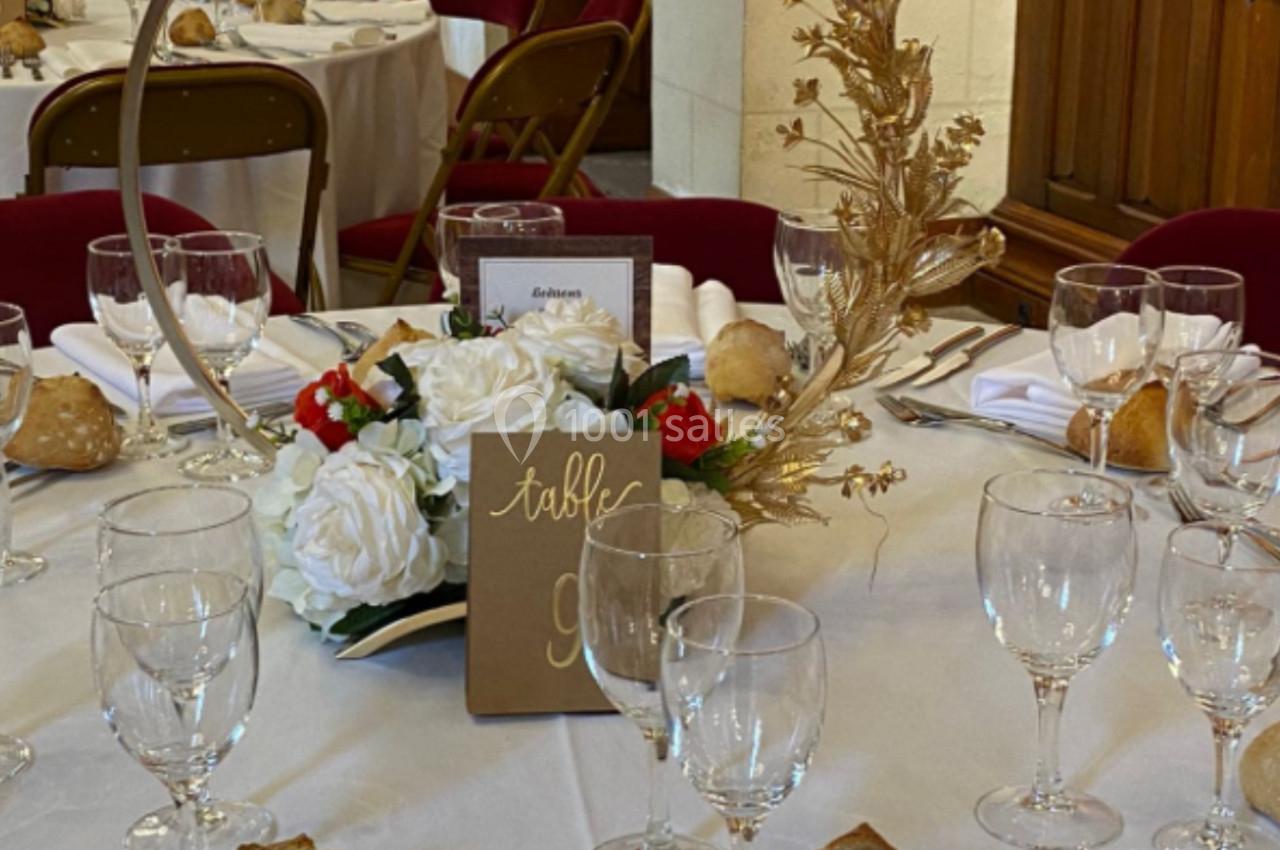 Table dressée pour un événement, avec nappes blanches, vaisselle élégante, centre de table floral et décor doré.
