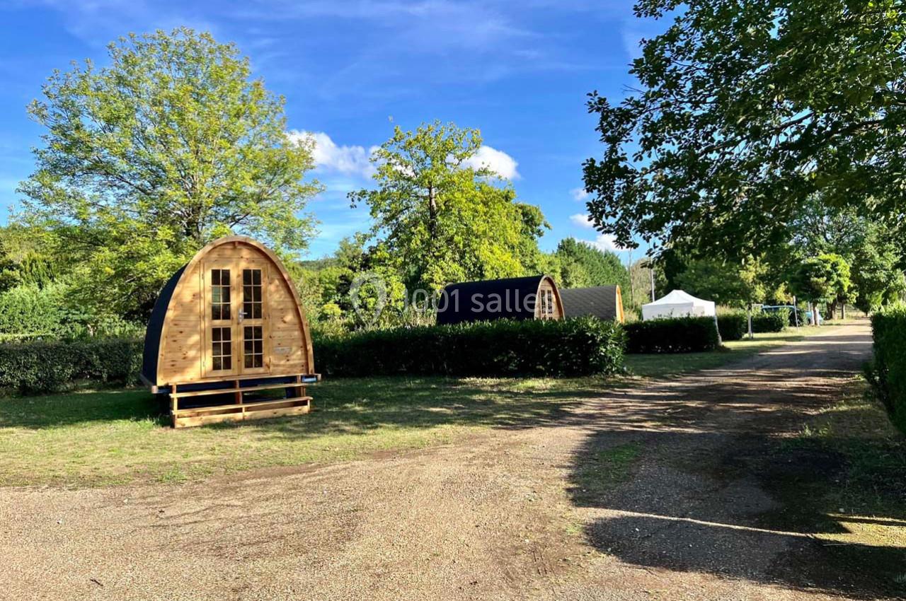 Deux cabanes en bois en forme d’arche dans un espace vert avec un chemin de gravier et des arbres environnants.