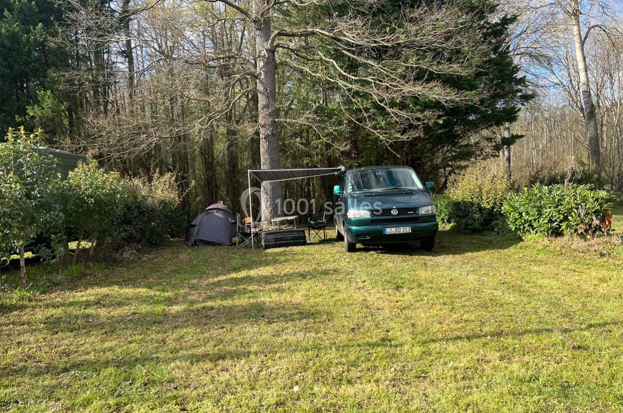 Un van vert, une tente et un espace de détente installés sur une pelouse entourée d'arbres.